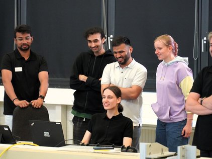 Sechs Teammitglieder stehen lachend hinter dem Arbeitstisch mit Laptops