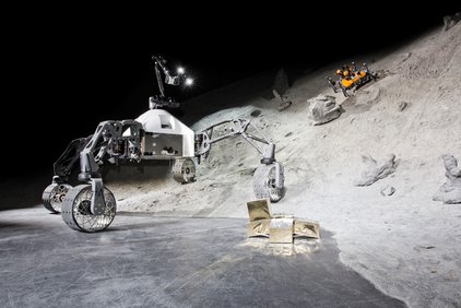 Die am Weltraumszenario beteiligten mobilen Systeme SherpaTT (links), Coyote III (orange, im Krater) mit aufgestecktem Manipulator und Basecamp mit aufgestecktem Payloadwürfel (im Vordergrund). (Foto: Florian Cordes, DFKI GmbH)