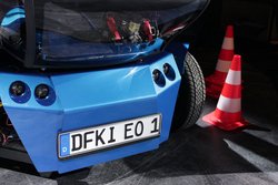 Front von EO smart connecting car mit einem von zwei Batteriefächern hinter dem Nummernschild (Quelle: Timo Birnschein, DFKI GmbH)